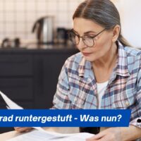 Pflegegrad runtergestuft: Was Betroffene jetzt wissen und tun müssen 5 Ältere Frau sitzt nachdenklich am Küchentisch und hält einen Bescheid der Pflegekasse in der Hand, dazu der Schriftzug „Pflegegrad runtergestuft – Was nun?