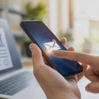 Hand tippt auf Smartphone-Benachrichtigung mit Briefsymbol, im Hintergrund unscharf ein Laptop mit digitalem Dokument, Symbolbild für den digitalen Steuerbescheid ab 2027
