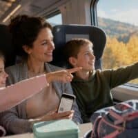Mutter mit zwei Kindern im ICE am Fensterplatz, die Kinder zeigen fröhlich auf die herbstliche Landschaft draußen