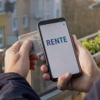 Hände halten einen Personalausweis an ein Smartphone, um sich mit der Online-Ausweisfunktion bei der digitalen Rentenübersicht anzumelden.