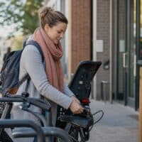 Mutter schließt morgens ihr Fahrrad mit Kindersitz vor einem Bildungszentrum ab, daneben eine Kreidetafel mit dem Wort NEUSTART