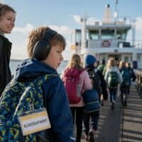 Grundschüler mit Gehörschutz-Kopfhörern geht mit seiner Begleiterin und der Klasse über einen Fähranleger an der Nordsee