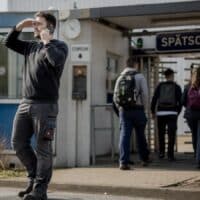 Schichtarbeiter in Arbeitskleidung telefoniert kurz vor Schichtbeginn vor dem Tor einer Produktionshalle