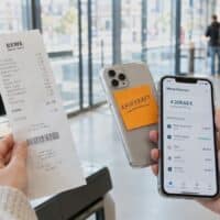 Hand hält an einer Supermarkt-Selbstbedienungskasse einen Kassenbon und ein Smartphone mit Haftnotiz „KAUFKRAFT“ – Symbolbild für den Kaufkraftverlust beim Regelsatz von 563 Euro