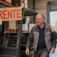 Lagerarbeiter Anfang sechzig wird an seinem letzten Arbeitstag in der Lagerhalle von Kolleginnen und Kollegen verabschiedet, am Gabelstapler hängt ein Schild mit dem Wort RENTE.