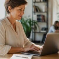 Frau mit Unterarmgehstütze schreibt am Laptop in einem hellen Büro eine Bewerbung mit Hinweis auf ihre Schwerbehinderung