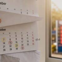 Hand reißt Kalenderblatt September ab, darunter markierte Termine im Oktober 2026, im unscharfen Hintergrund eine Tankstelle als Symbol für den neuen Tankrabatt