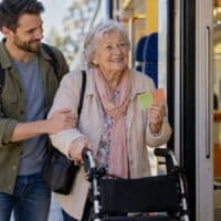 Ältere Frau mit Rollator und Schwerbehindertenausweis steigt mit Begleitperson in einen Regionalzug